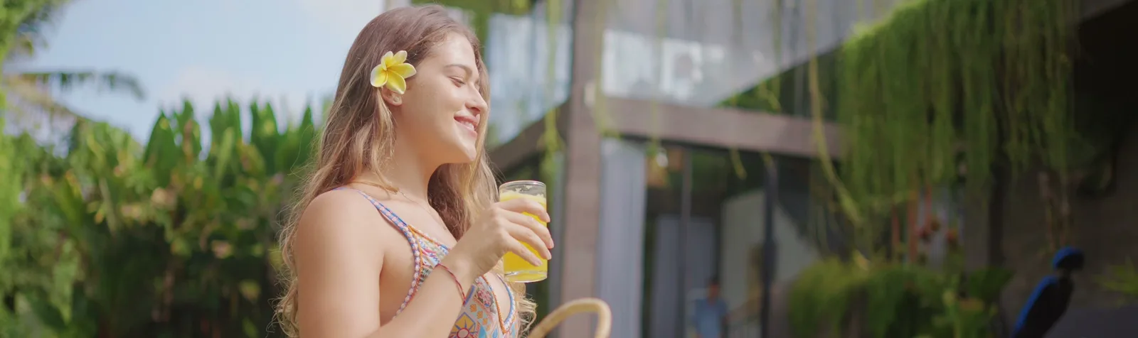 A woman with a frangipani flower in her hair, drinking by the pool at the Zouk Village.